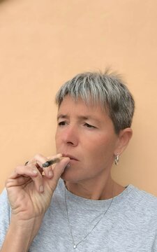 Adult woman with short gray hair, with a lost look smoking a cigarette. Relaxing after a stressful day. Alternative therapy. Treating insomnia