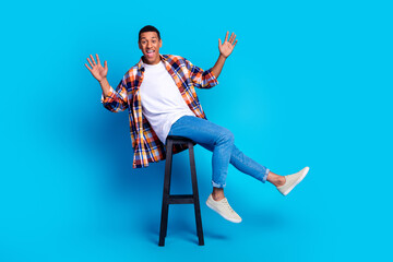 Full length photo of nice young man sit stool rejoice wear shirt isolated on blue color background