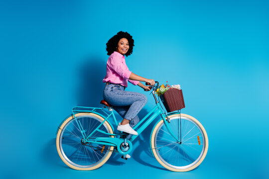 Full size side profile photo of cute woman wear pink shirt jeans pants driving bicycle to empty space isolated on blue color background