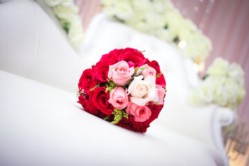 Wedding bouquet of the bride in red tones is on a white  chair. Flowers for wedding reception.