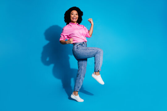 Full length profile portrait of pretty young woman raise fists empty space wear pink shirt isolated on blue color background