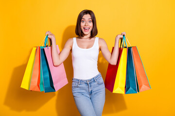 Photo portrait of attractive young girl hold excited shopping bags wear trendy white outfit isolated on yellow color background