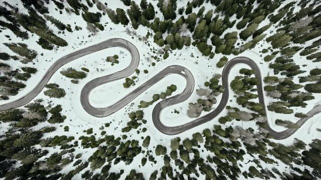Serpentine road in Passo Giau in the Dolomites, car traveling across the Snake road with snow in the winter season, aerial footage