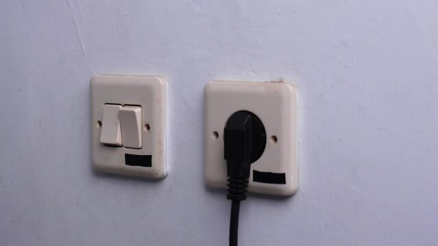 hand pressing light switch button with electrical outlet on a wall
