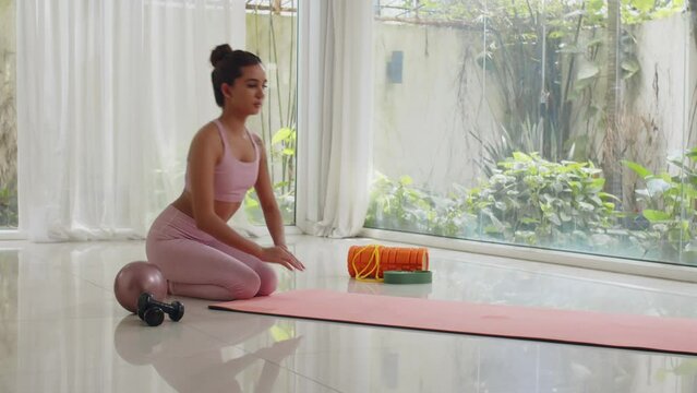 Wide shot of young Asian gen Z sportswoman rolling out yoga mat while working out indoorsWide shot of young Asian gen Z sportswoman rolling out yoga mat while working out indoors