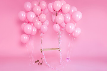 Romantic swing decorated with bunch of pink balloons on a pink background in the studio. Birthday and wedding celebration concept. Decor for holidays and events.