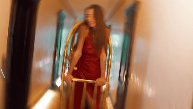 Two sexy women in red dresses ride on a golden luggage trolley in a hotel. Fashion shooting concept