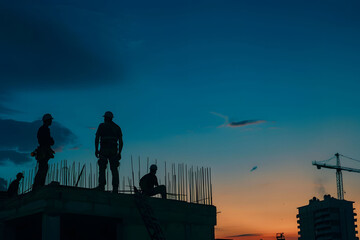 Silhouette of a construction worker and team working together on a building site at sunset with a warm sky background.