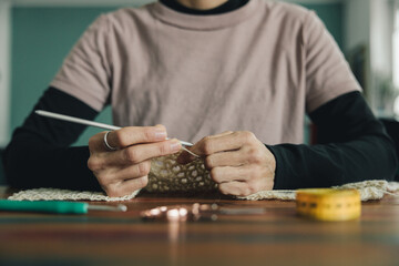 A person is knitting a sweater with a crochet hook, the sweater is white