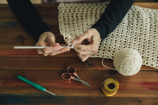 High angle view of a woman is crocheting a blanket on a wooden table, she is using a crochet hook, tape measure and scissors