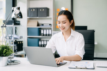 Obraz na płótnie Canvas Asian Businesswoman Analyzing Finance on Tablet and Laptop at Office Desk tax, report, accounting, statistics, and analytical research concept