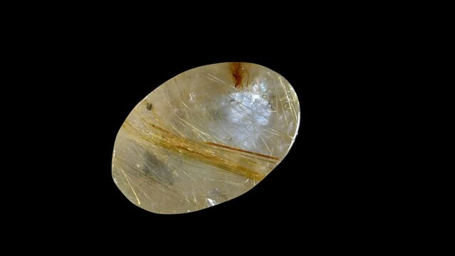 Rutilated quartz - clear quartz containing needle-like inclusions of rutile - rotating slowly against a black background.