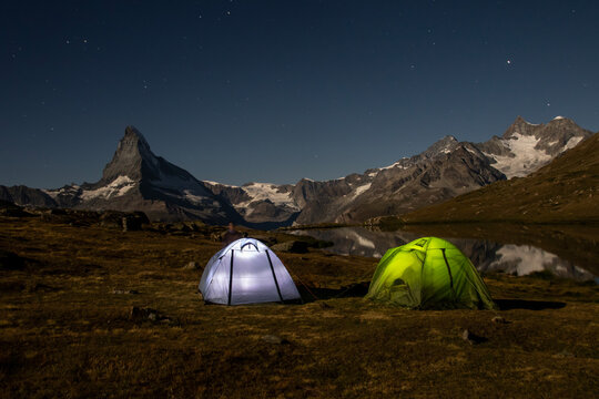 Two vibrant tents pitched beside Stellisee Lake at 2600 meters under a star-studded sky with the Matterhorn in Switzerland standing majestic in the background