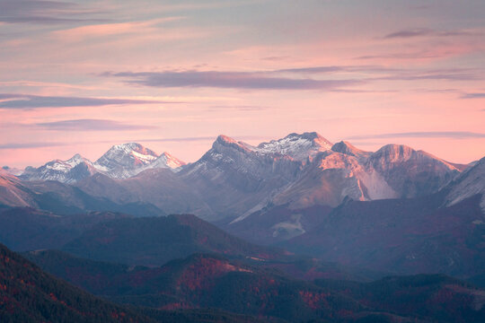 The last light of day casts a pink glow over the snow-capped peaks of the Pyrenees, with the Selva de Irati forest in autumnal hues below