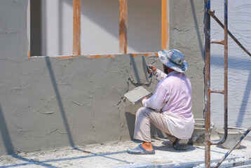 Asian builder is plastering cement wall inside of room in house construction site
