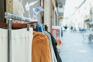 A selection of winter clothing displayed on an outdoor rack during a sidewalk sale, with the bustling city as a backdrop