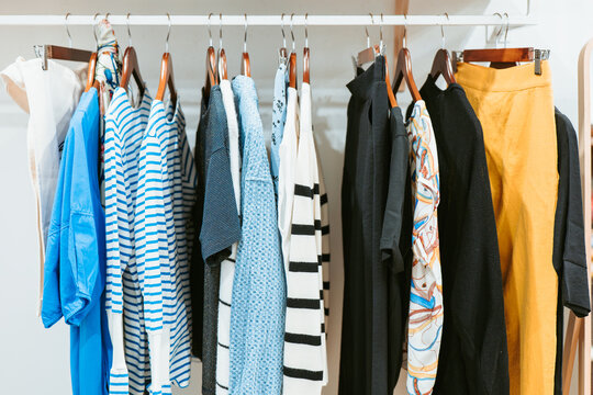 An array of textured garments ranging from stripes to solid colors hangs from a wooden rack in a chic boutique setting