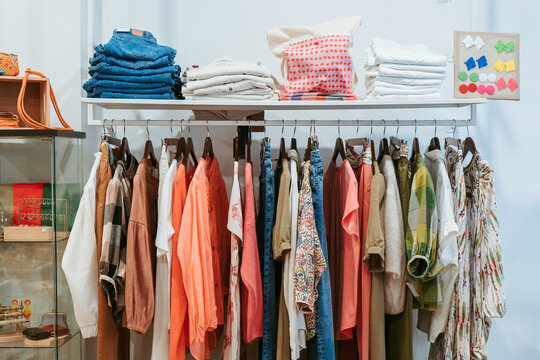 A colorful assortment of clothing items, including denim and patterned apparel, displayed on a metal rack with neatly folded piles on top