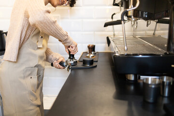 Hispanic woman barista tamping coffee at espresso machine