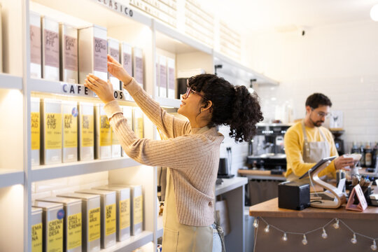 Cheerful employee restocking shelves in modern cafe