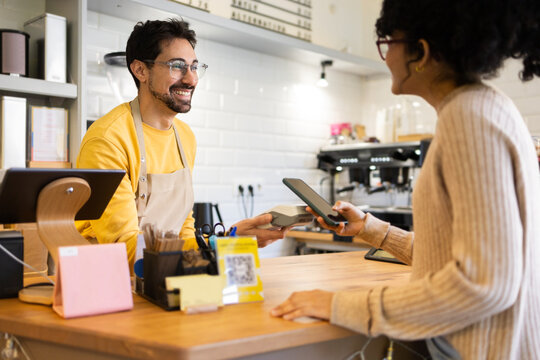 Cheerful barista accepting mobile payment in cafe