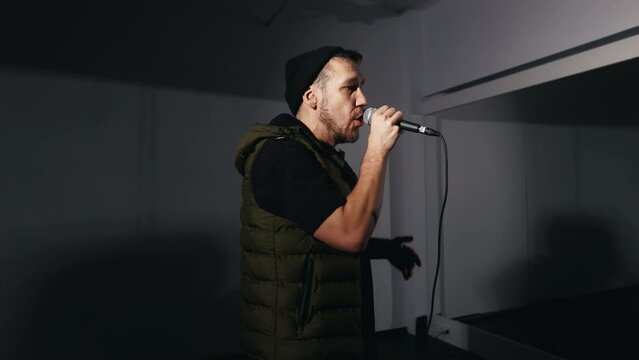 Emotional delivery: Male artist or rapper conveys emotion, singing into microphone and gesturing with arm in dark recording space