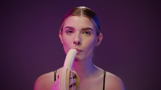 Sexy woman eats a piece of a banana, concept oral sex, purple studio light