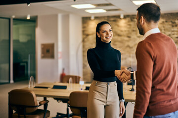 Businesswoman and businessman shaking hands at the office, smiling. - 775825955
