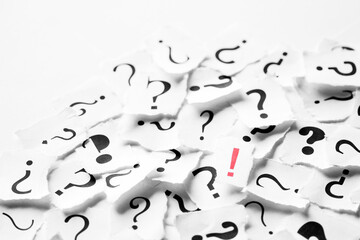 Pile of question mark signs scattered around with one red exclamation symbol in the center....