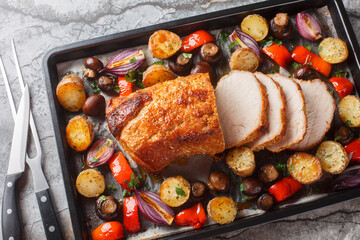 Honey baked pork loin with potatoes, onions, bell peppers and mushrooms close-up on a baking sheet...