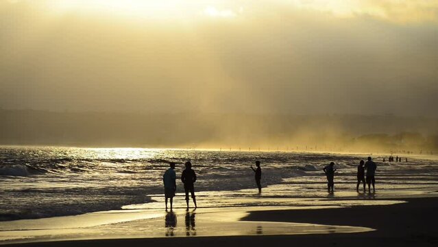 People relaxing along the beach at sunset, silhouettes of people at dusk