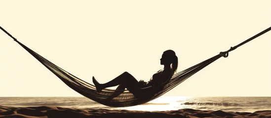 Tuinposter silhouette of woman relaxing in hammock on the beach © haizah