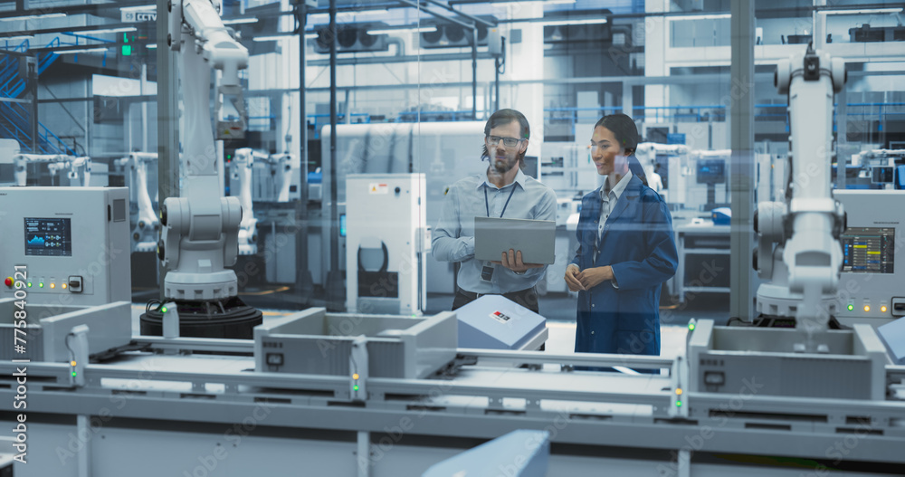 Poster two diverse engineers standing in a factory, using laptop at an electronics factory. female and male