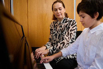 Teenager schoolboy playing piano with his teacher during individual music lesson at home. Musical...
