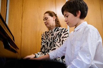 Confident teenage boy pianist musician creating the rhythm of melody, touching white and black keys...