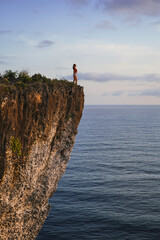 Young Woman Standing On The Edge Of The Cliff Watching At The Ocean In Bali, Indonesia
