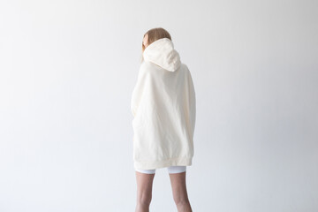 Beautiful blonde woman posing in white hoodie and leggings posing against white background. Posing with his back.