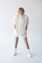 Beautiful blonde woman posing in white hoodie and leggings posing against white background