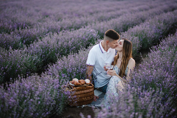 Couple sits in lavender field on romantic evening at sunset. Male kisses female. Man hugs woman...