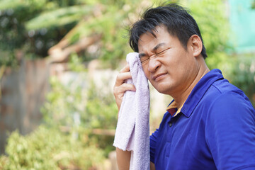 Asian man feel headache and unwell from hot weather condition,  use cool wet cloth to wipe face for...