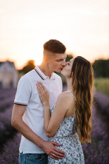 Romantic young couple kissing together in purple lavender field. Male embracing female enjoying romantic time in sunset. Beautiful woman hugs man among violet flowers with sunlight on summer day.