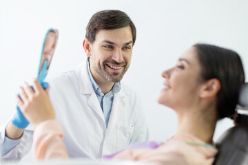 Lady patient holding mirror looking at teeth treatment result during dental check up in dentist cabinet, side view
