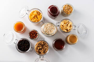 Obraz na płótnie Canvas food storage and eating concept - close up of jars with oat, corn flakes, granola, cookies and spreads on white background