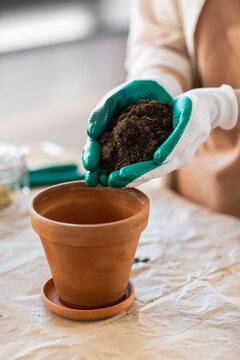 people, gardening and housework concept - close up of woman in gloves pouring soil to flower pot at home