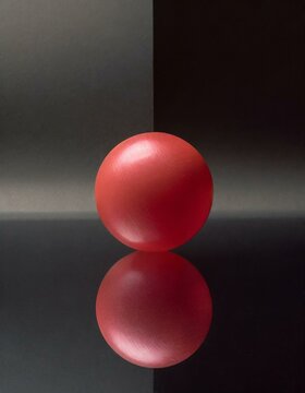 A glossy red sphere on a reflective black surface, creating a crisp, dual image that speaks to symmetry and introspection