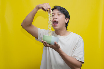 A young Asian man is pinching and swallowing noodles with his hingers in deep satisfaction...