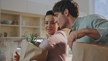 Spouses taking out products from paper package at kitchen. Family unpacking food - obrazy, fototapety, plakaty
