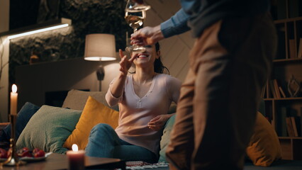 Romantic husband bringing wine to smiling wife sitting couch. Couple having date