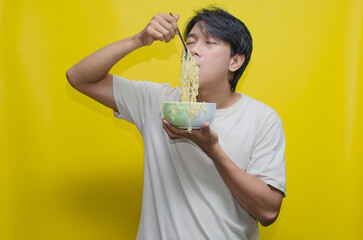 A young Asian man is devouring noodles with his hungry expression turning into one of deep satisfaction.