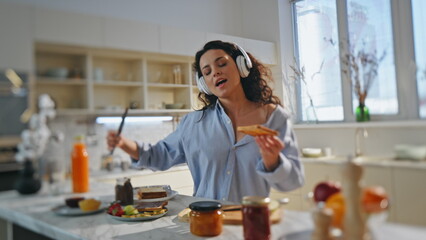 Girl headphones cooking breakfast at kitchen. Woman singing along favorite song